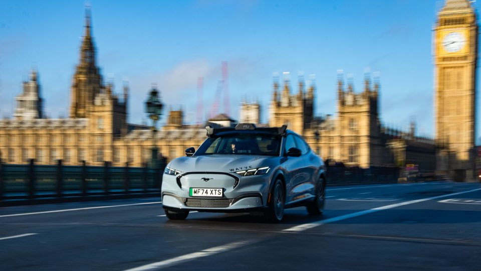 A grey SUV driving across a bridge in a city with the sun illuminating Big Ben in the background.