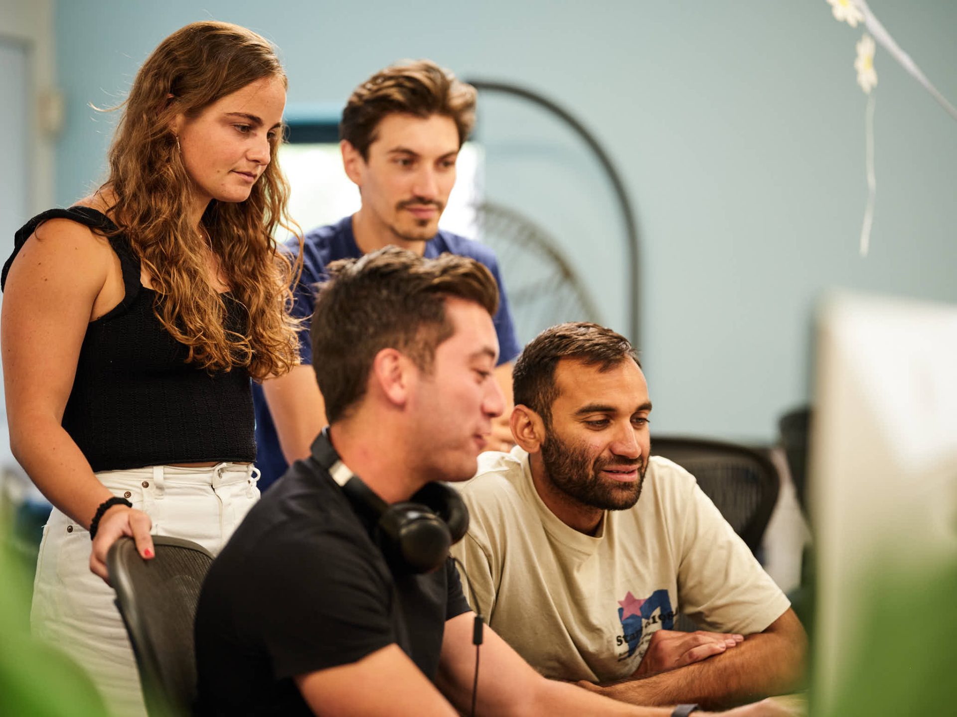 four people gathered around a computer screen in an office