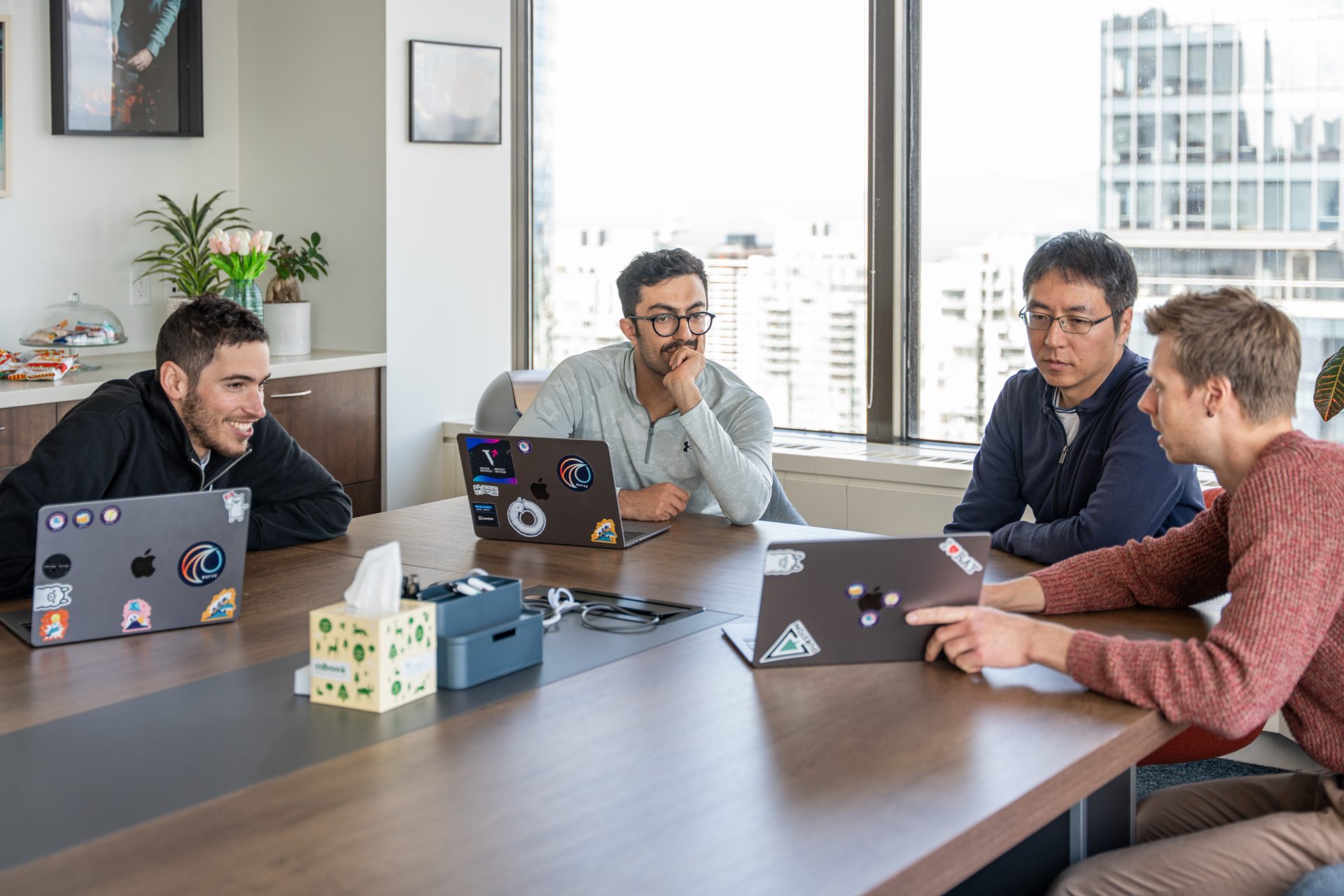 four people sat around a table with laptops during a meeting